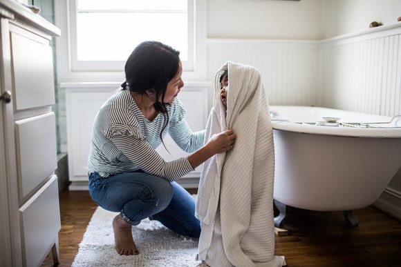 Adult and child in a bathroom, with child covered by towel.