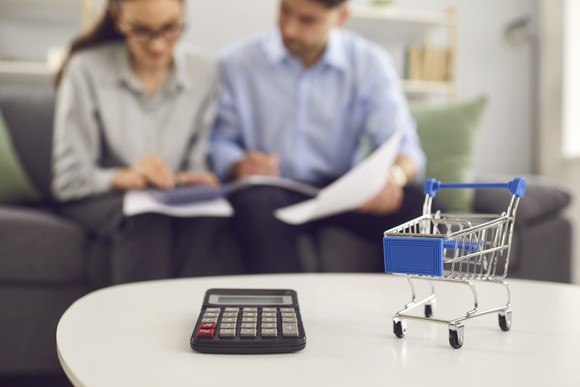 A small shopping basket and a calculator with two people in the background.