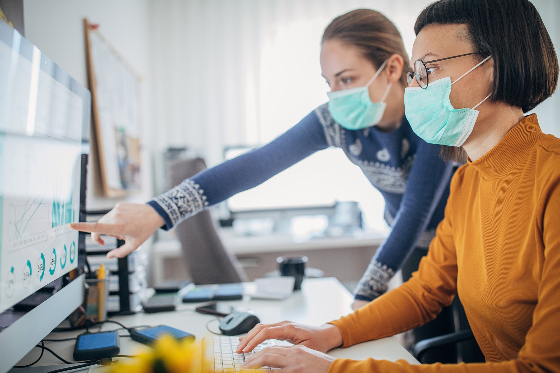 Two work colleagues collaborating in the office with masks.
