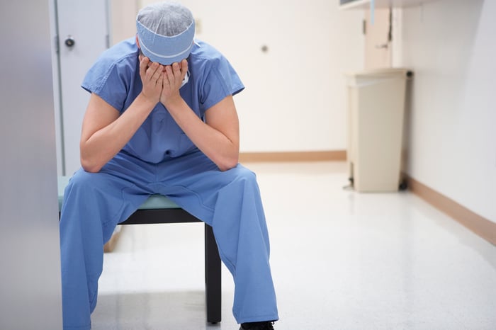 Doctor seated with head in hands.