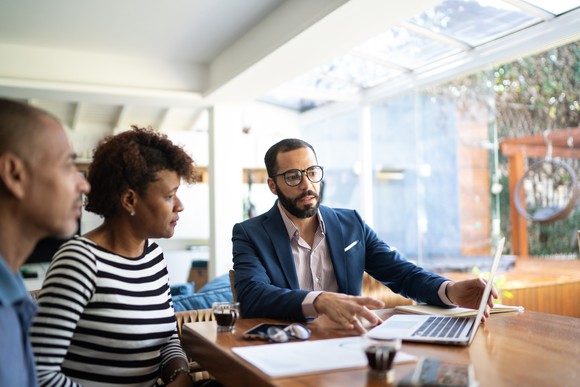 Three people look at a laptop.