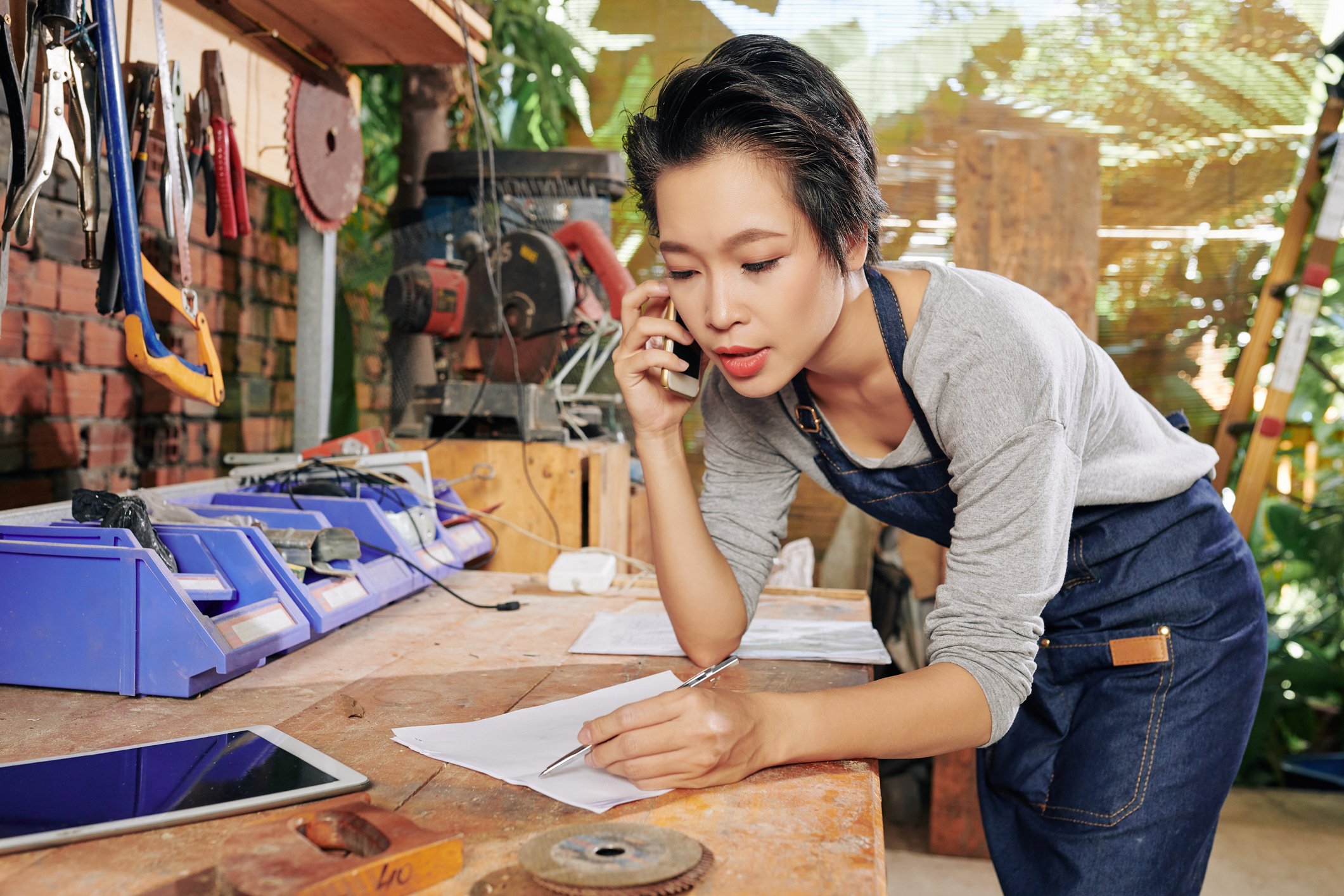 A woman using a mobile phone and writing on a paper in a studio.