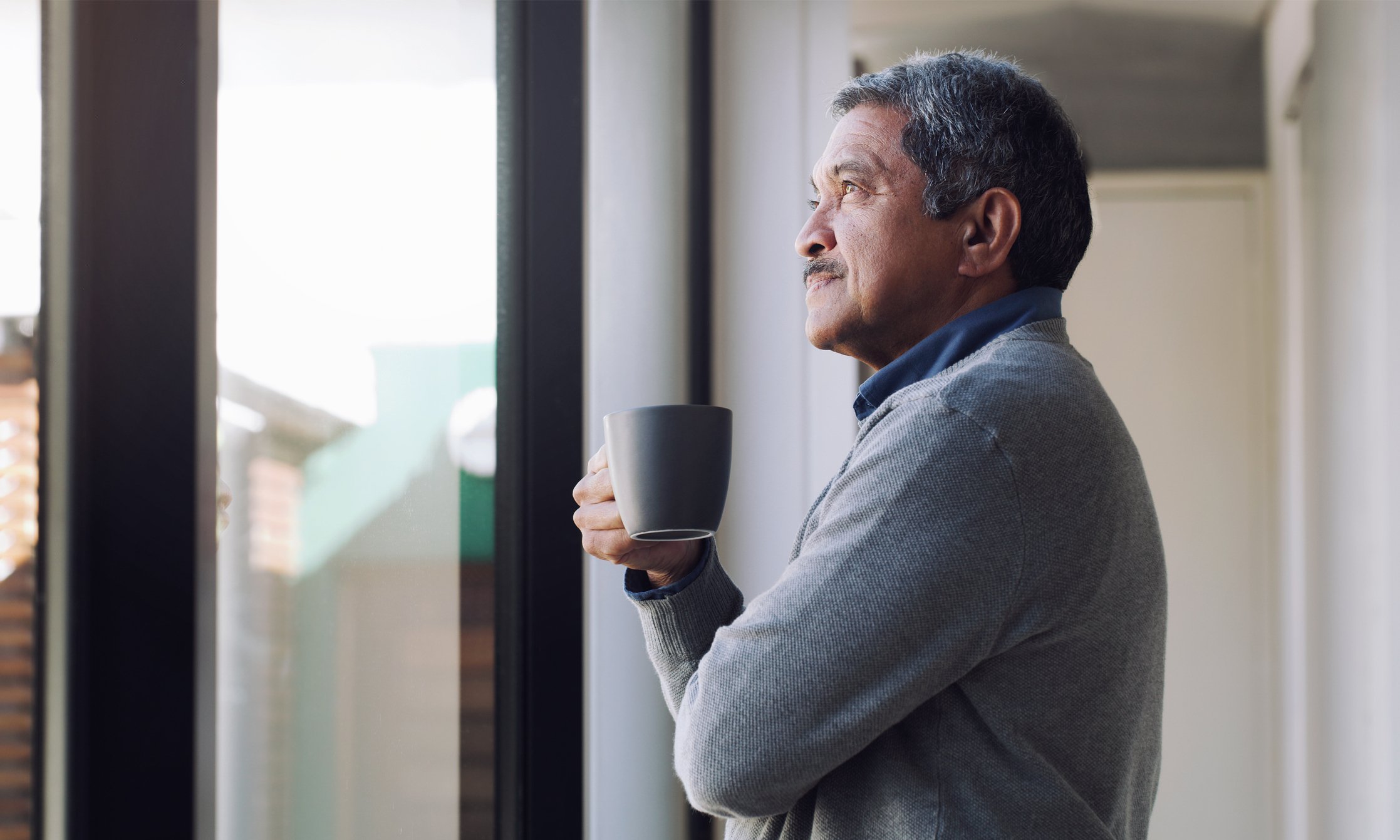 Person holding a cup of coffee looking out the window. 