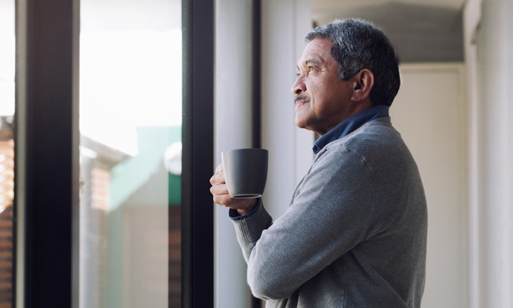 Person holding a cup of coffee looking out the window. 