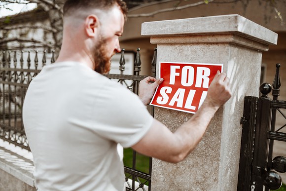 Person putting for sale sign on house.