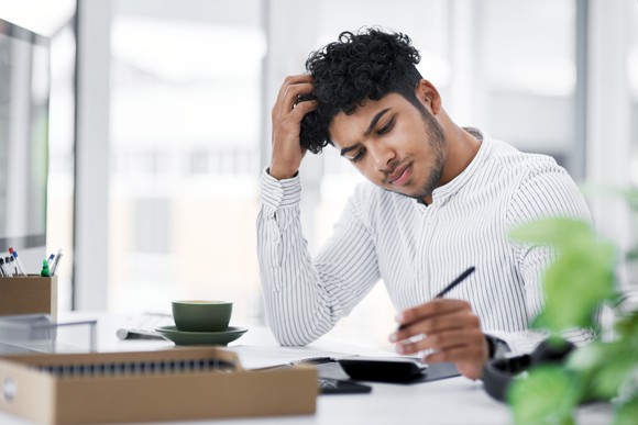 A person frowns over books and papers on the desk.