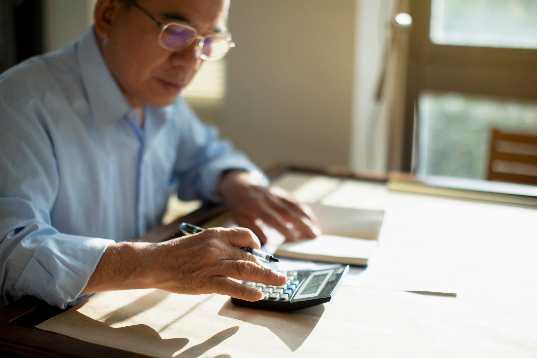 Person typing on calculator with papers at desk.