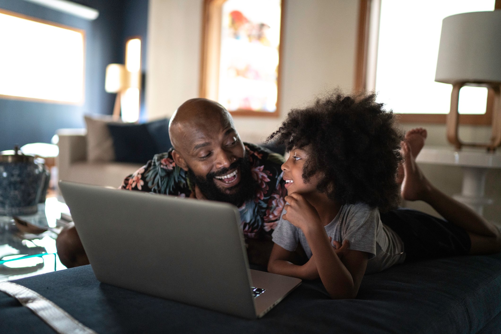 A father and daughter watch a show together on a laptop.