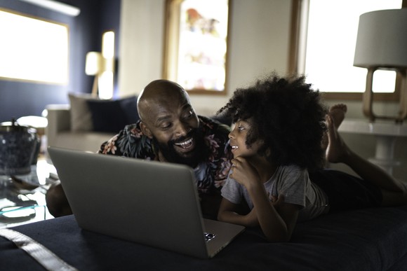 A father and daughter watch a show together on a laptop.