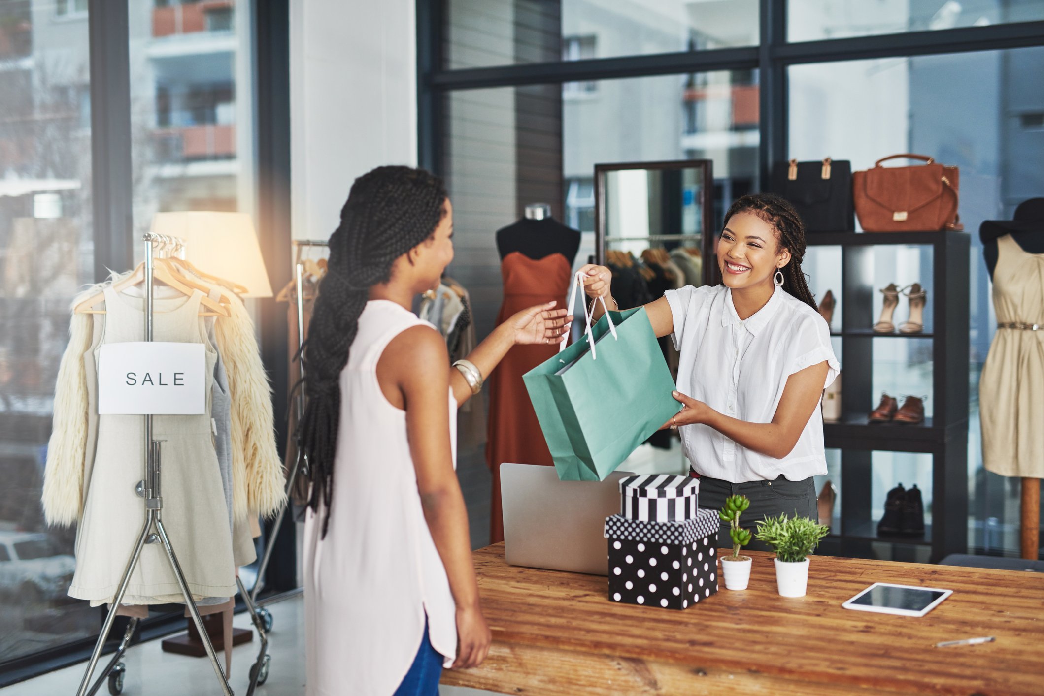 Person behind counter hands a shopper a shopping bag.
