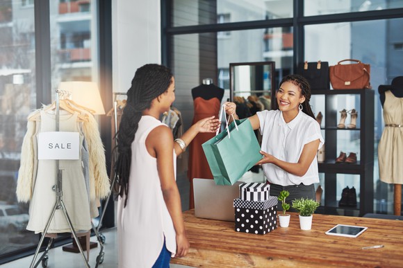 Person behind counter hands a shopper a shopping bag.