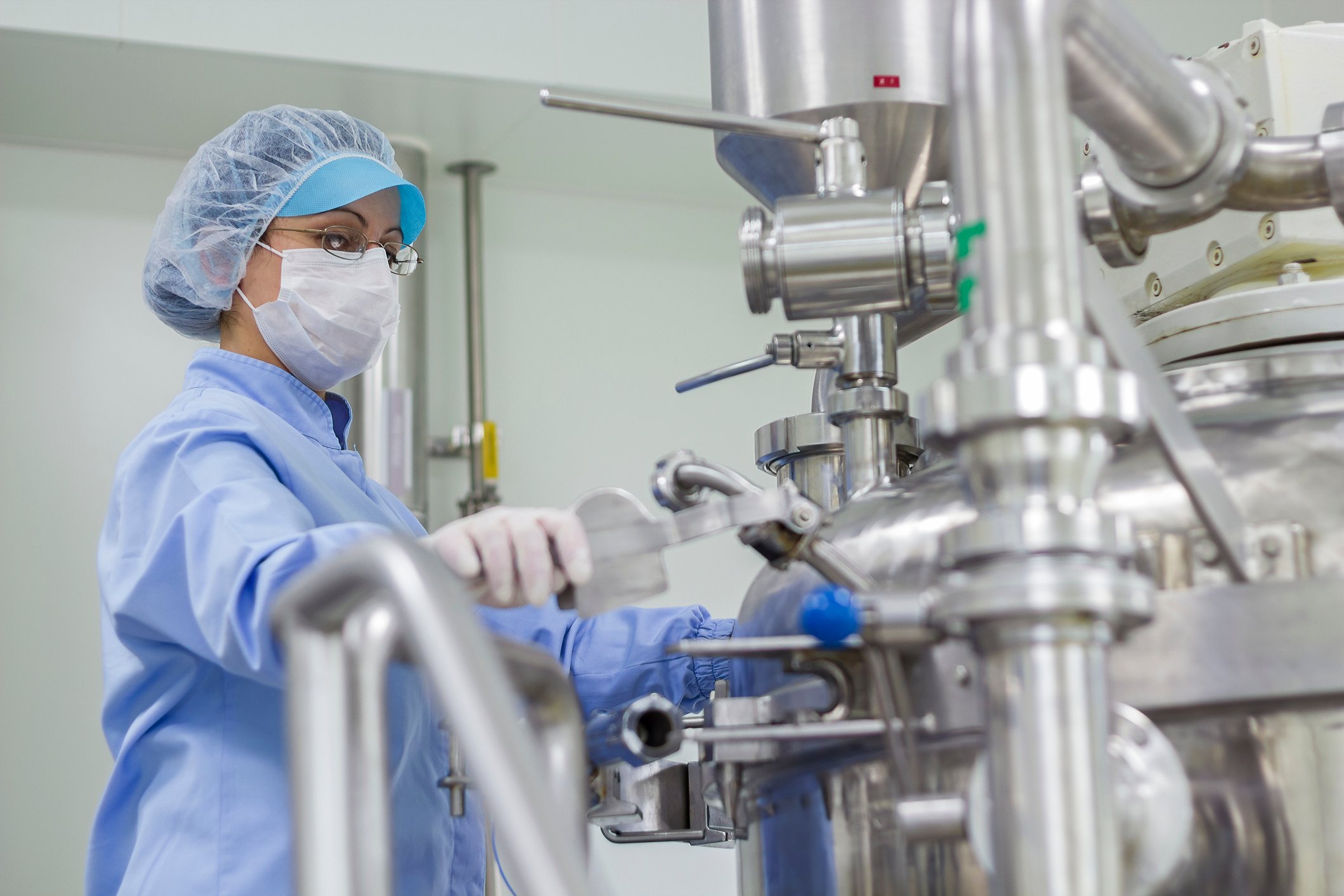 A worker wears a face mask while working on a machine in a pharmaceutical factory.