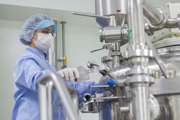 A worker wears a face mask while working on a machine in a pharmaceutical factory.