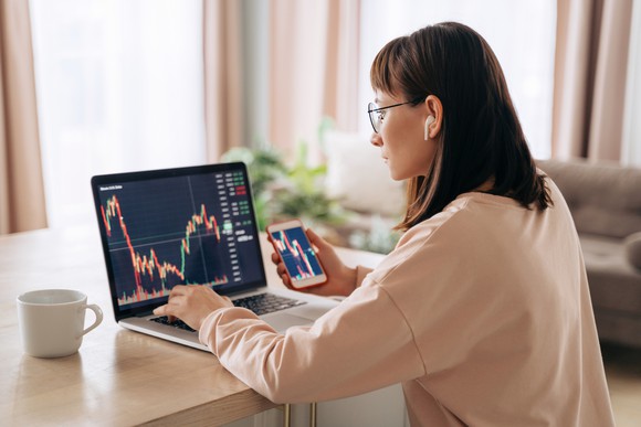 A person is looking at stock charts on a laptop and smartphone. 