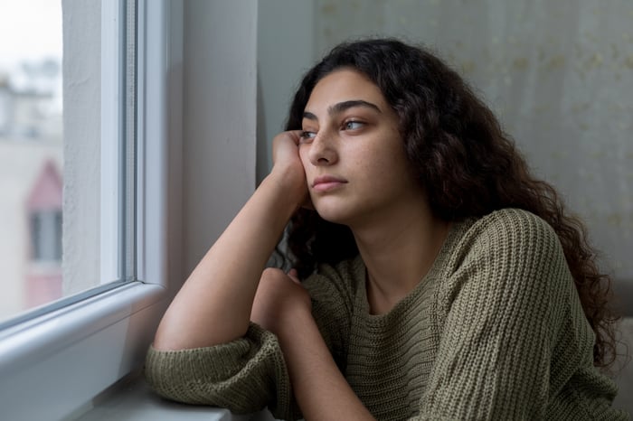 A person sitting down and looking forlornly out the window.