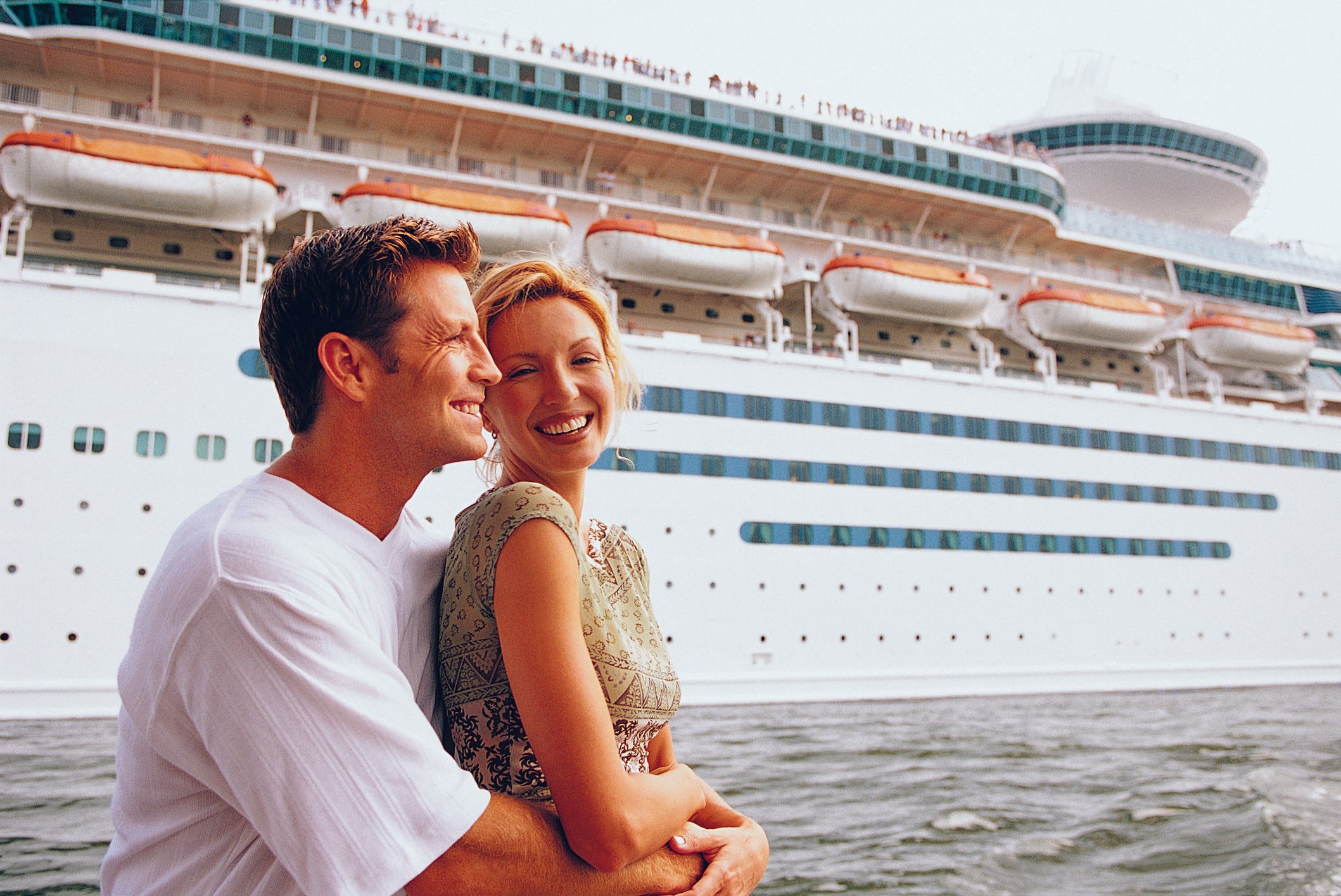Smiling couple embraces next to a cruise liner.