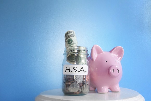 Jar stuffed with U.S. coins and currency, labeled "H.S.A." next to a piggy bank. 