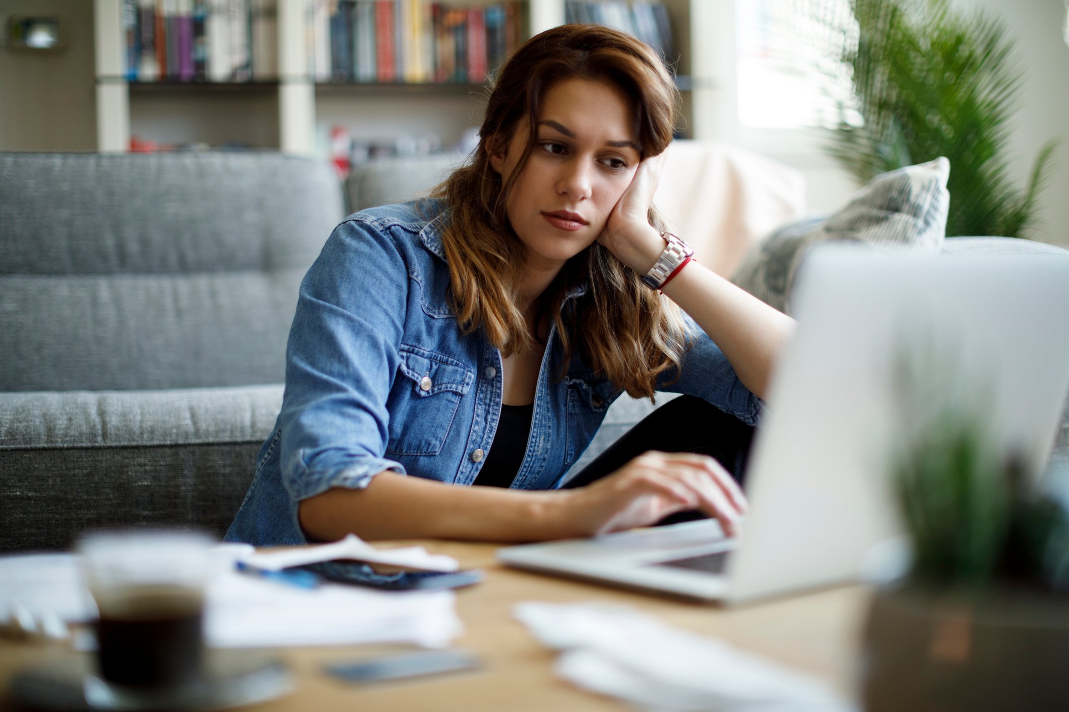 A person looks at a laptop, resting their head on their hand.