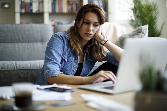 A person looks at a laptop, resting their head on their hand.
