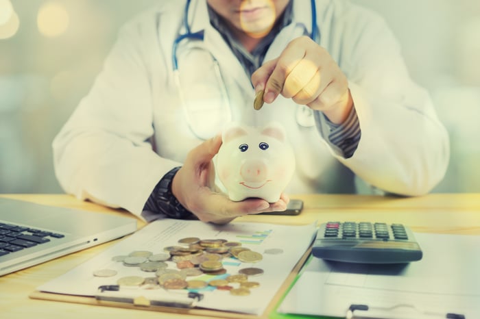 Doctor inserting a coin inside a piggy bank.