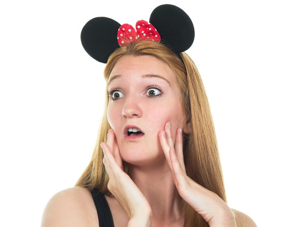 A person wearing black mouse ears puts their hands to their face.