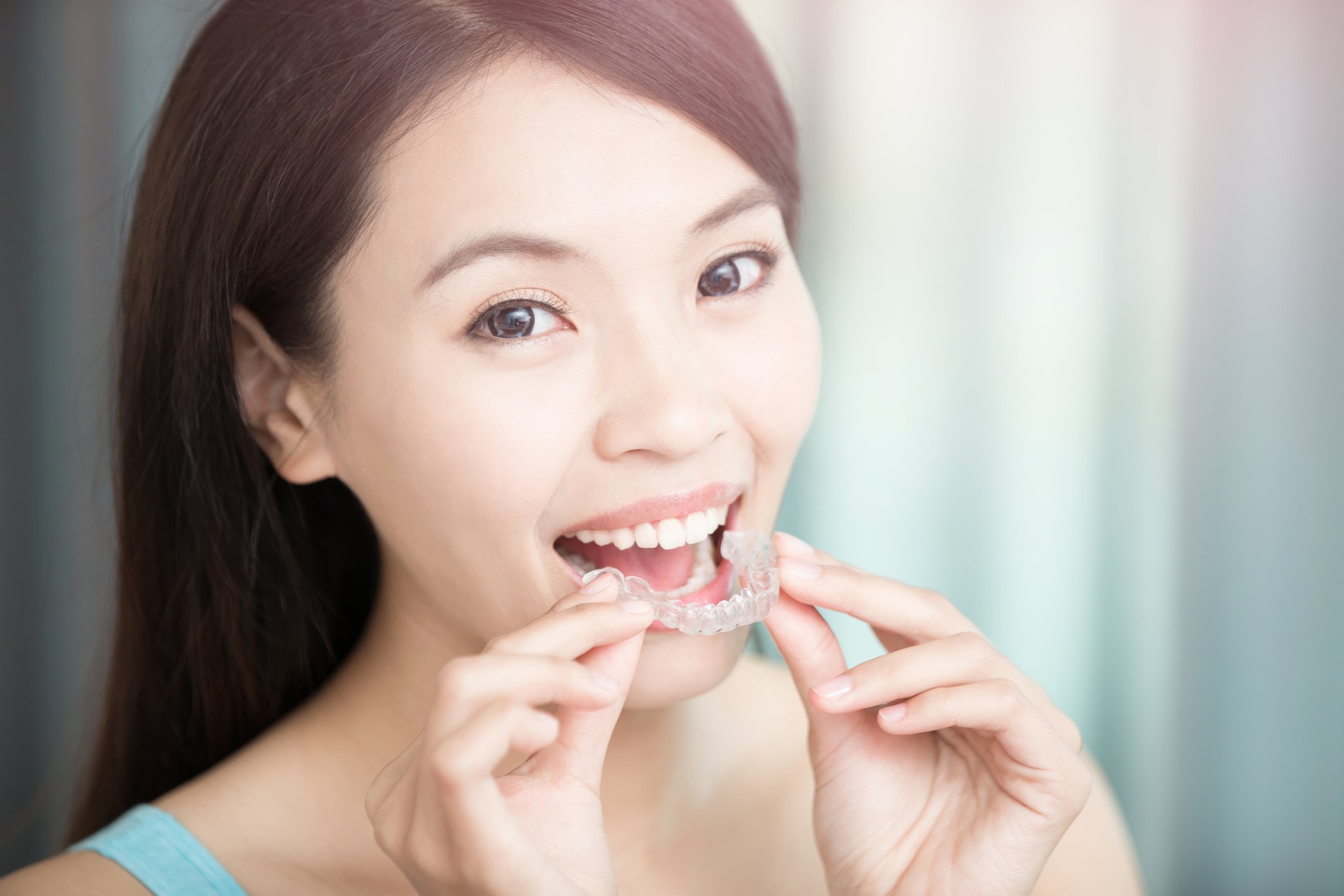A person smiling while putting in dental aligners.