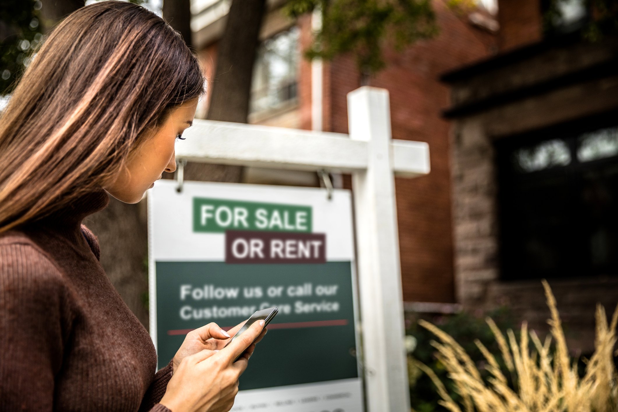 A person typing information from a "For Sale or Rent" sign into a phone.