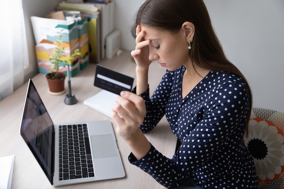 Stressed woman at a laptop, holding a payment card.