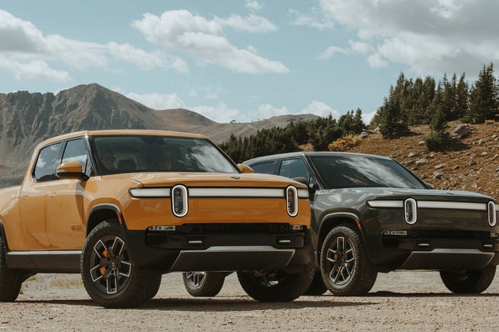 Two Rivian R1T pickup trucks parked in a rugged outdoor environment. 