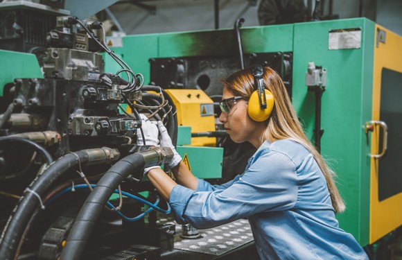 A lady wears personal protective equipment while working on a machine on a production line. 