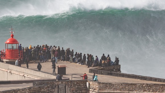A group of people standing in front of a huge wave.