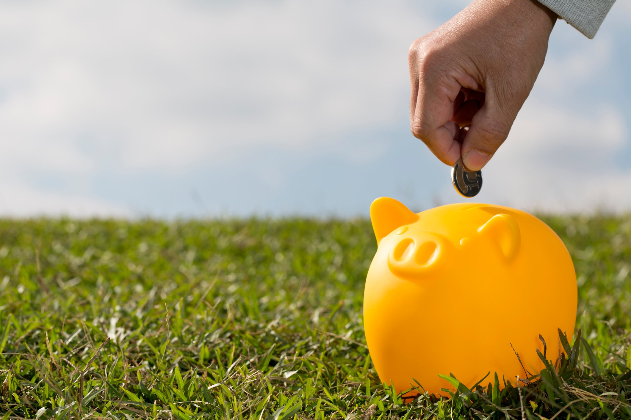 A hand putting a coin in a yellow piggy bank.