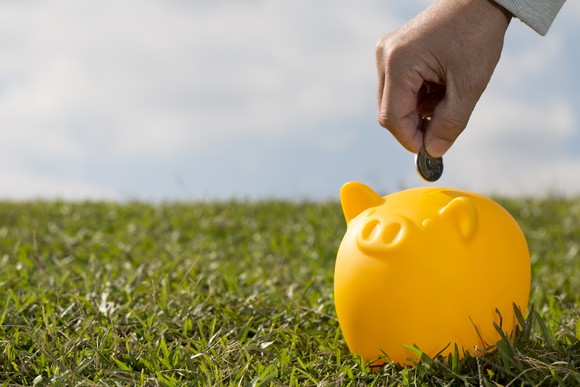 A hand putting a coin in a yellow piggy bank.