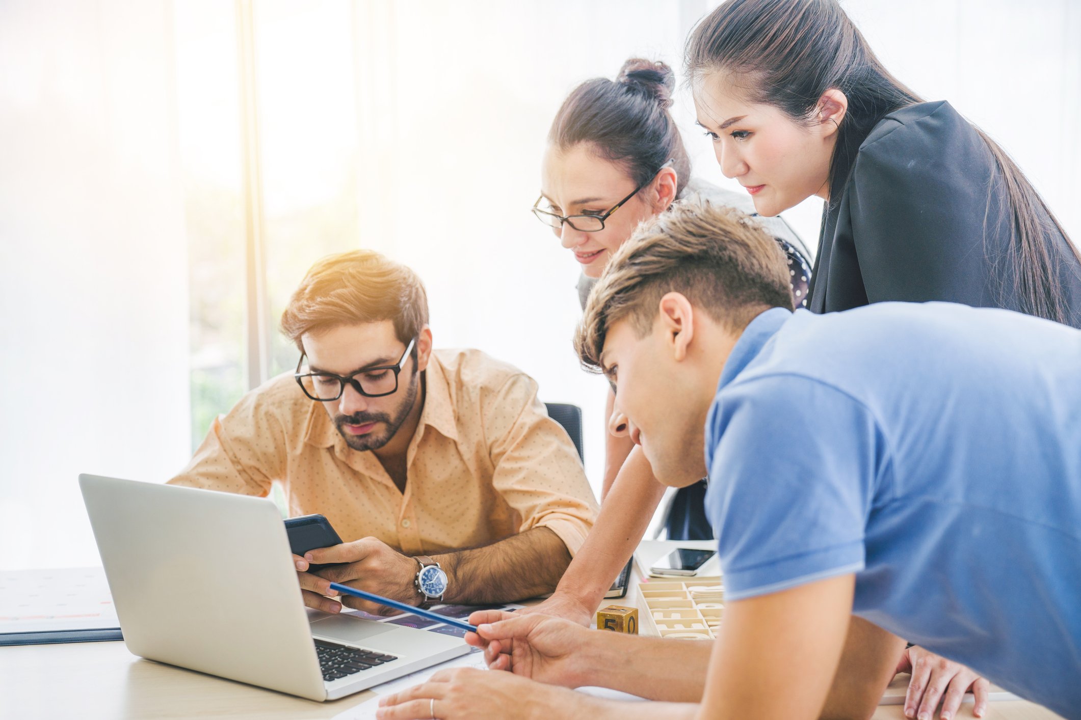 A group of young investors is gathered around a computer.