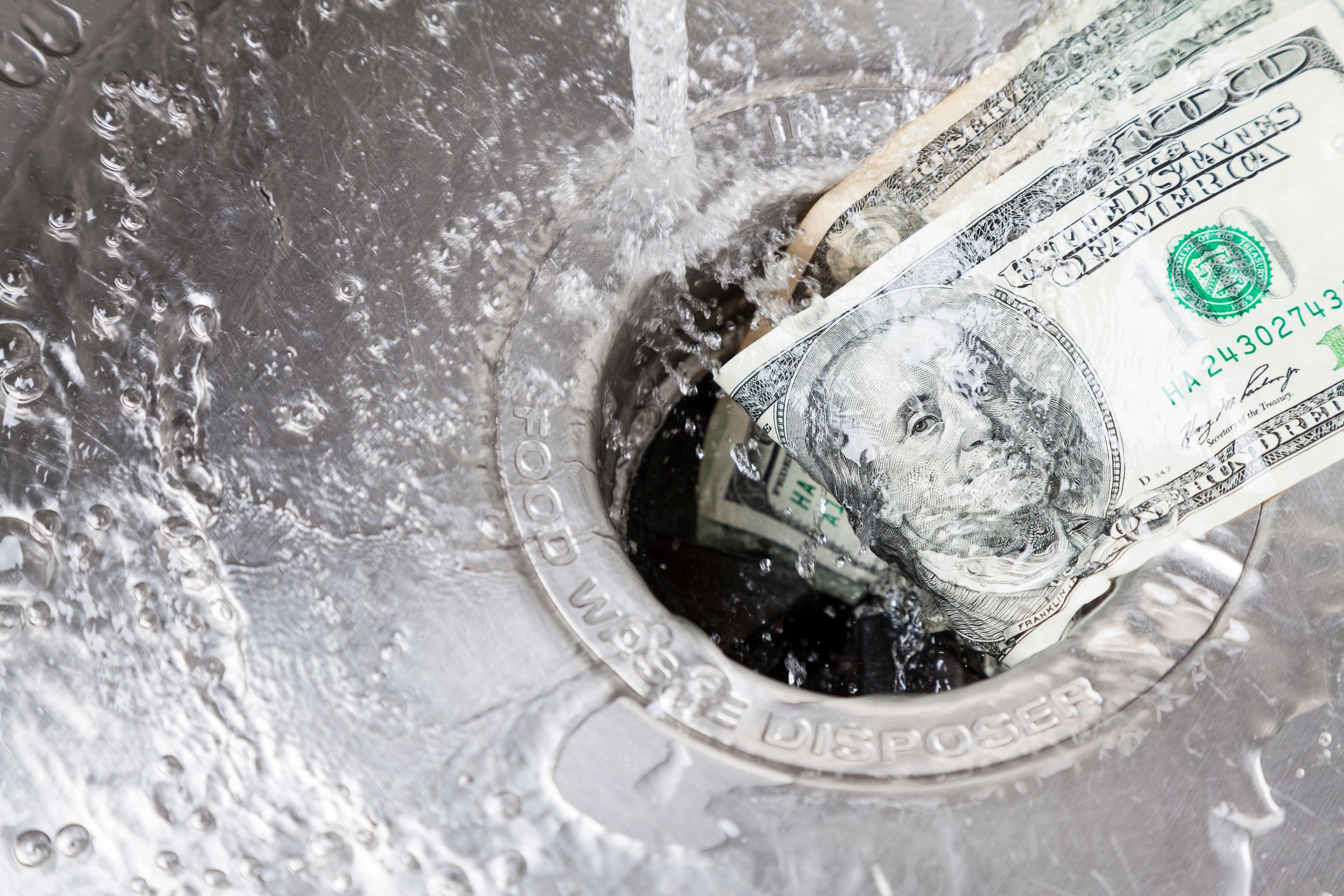 Hundred-dollar bills being washed down a drain.