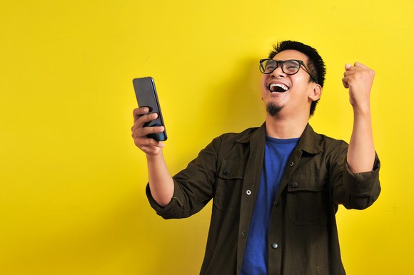 A person holding a phone while looking up and cheering.