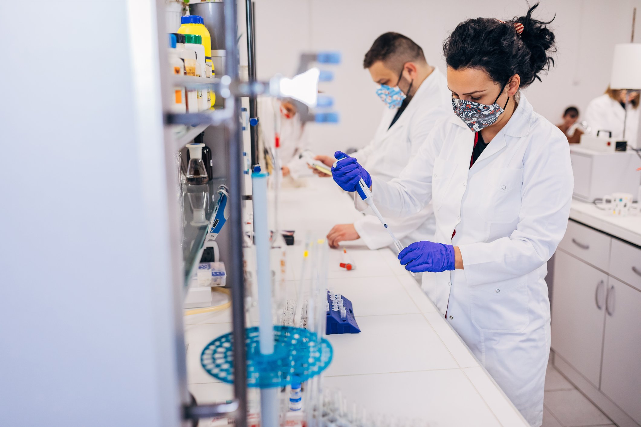 A pair of biotechnology researchers work with samples in test tubes while standing at a laboratory bench.