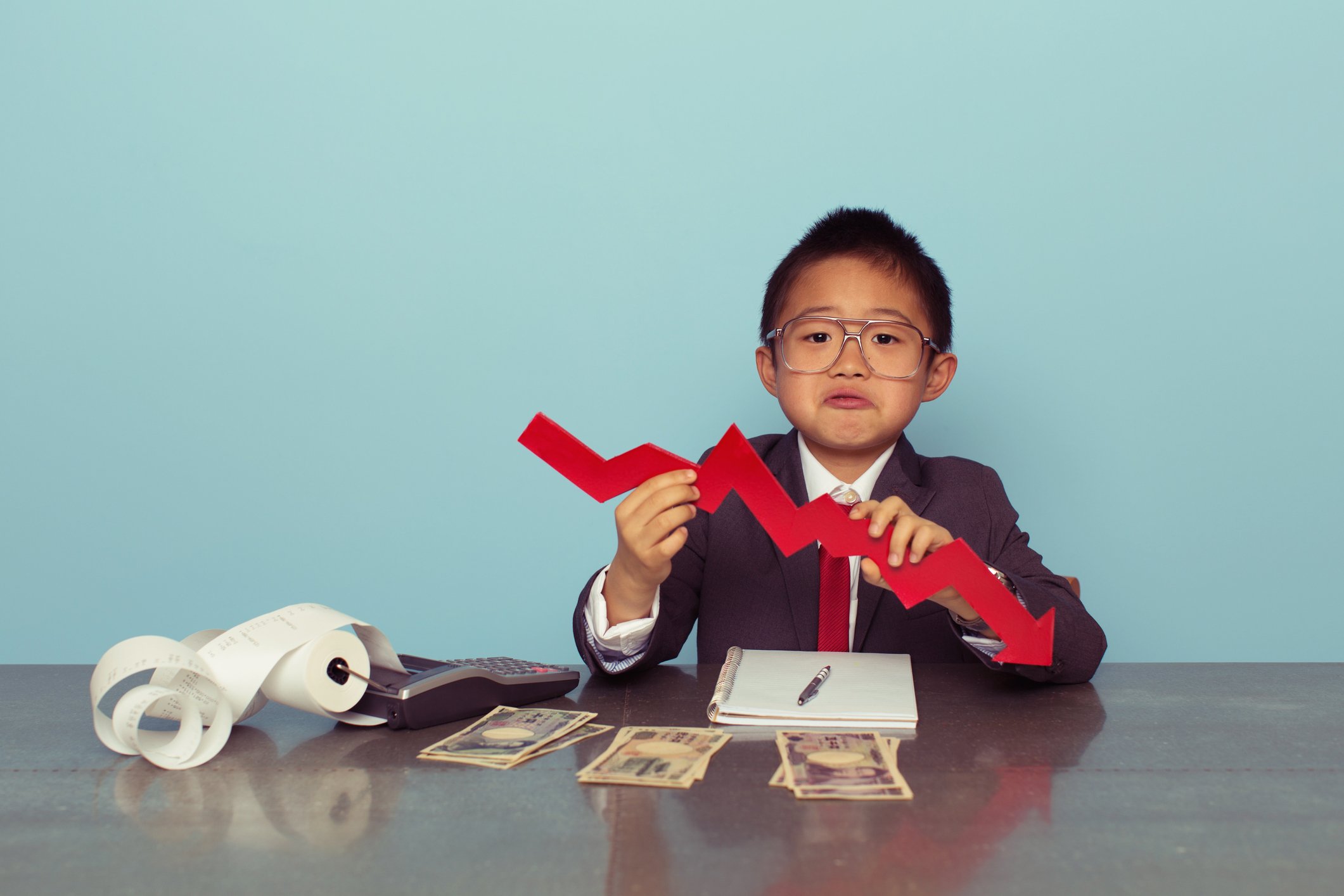 A child holds a declining chart in front of piles of money.