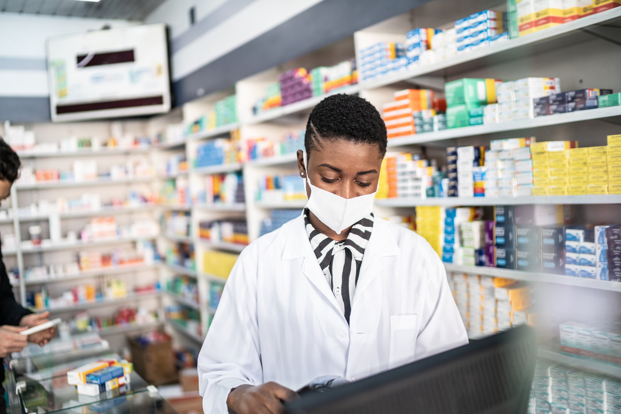 A pharmacist consults a computer while standing in the back of a pharmacy.