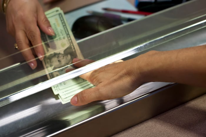 U.S. currency being exchanged across a bank teller window.