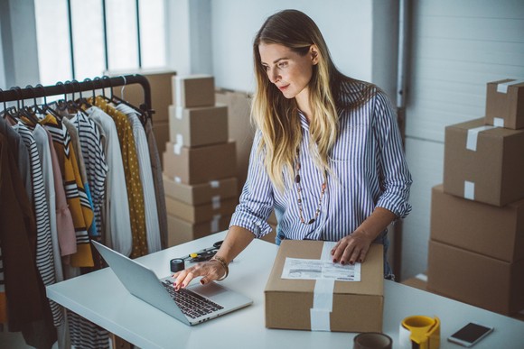A person stands in front of a desk with a laptop and a package on it.