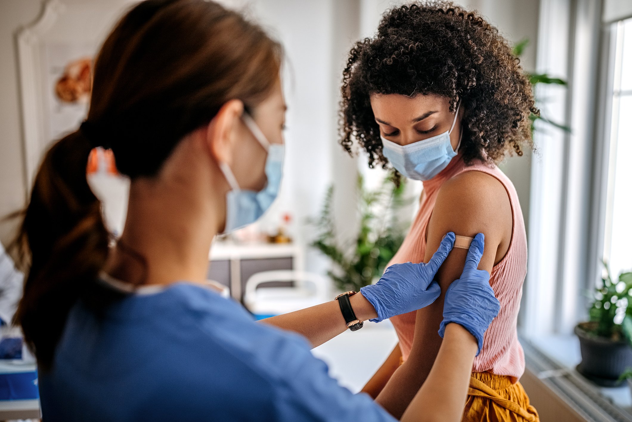 A healthcare worker presses a bandage on the arm of a patient in a medical office following vaccination.