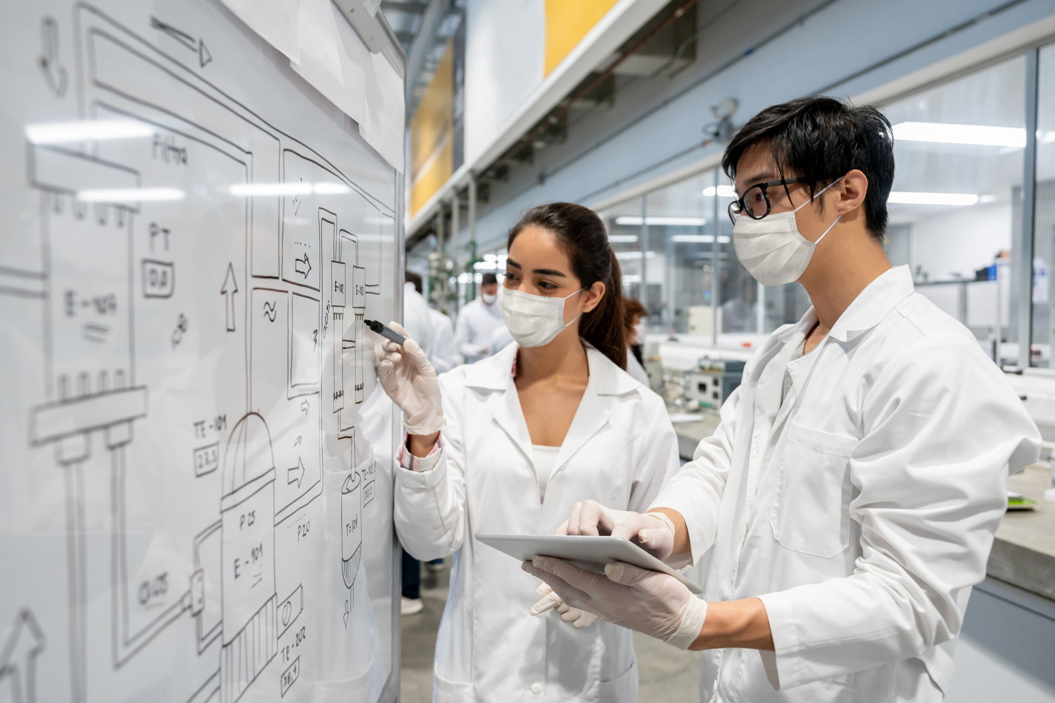 Two scientists standing in front of a board in a lab.