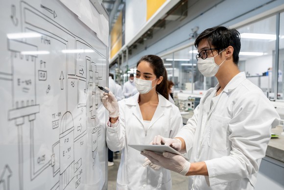 Two scientists standing in front of a board in a lab.