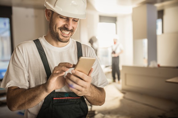 Construction worker in home remodel smiling at phone.