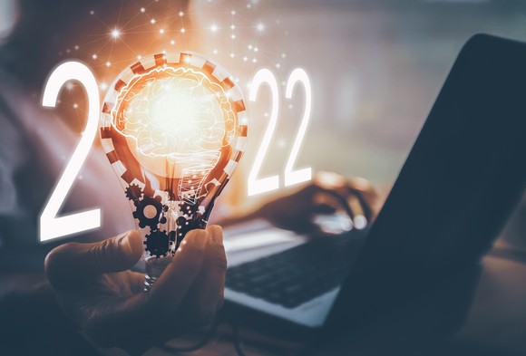 Person using a laptop while holding a lightbulb forming the zero in 2022.