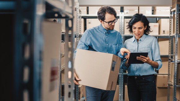 Two people in a warehouse with boxes in it.