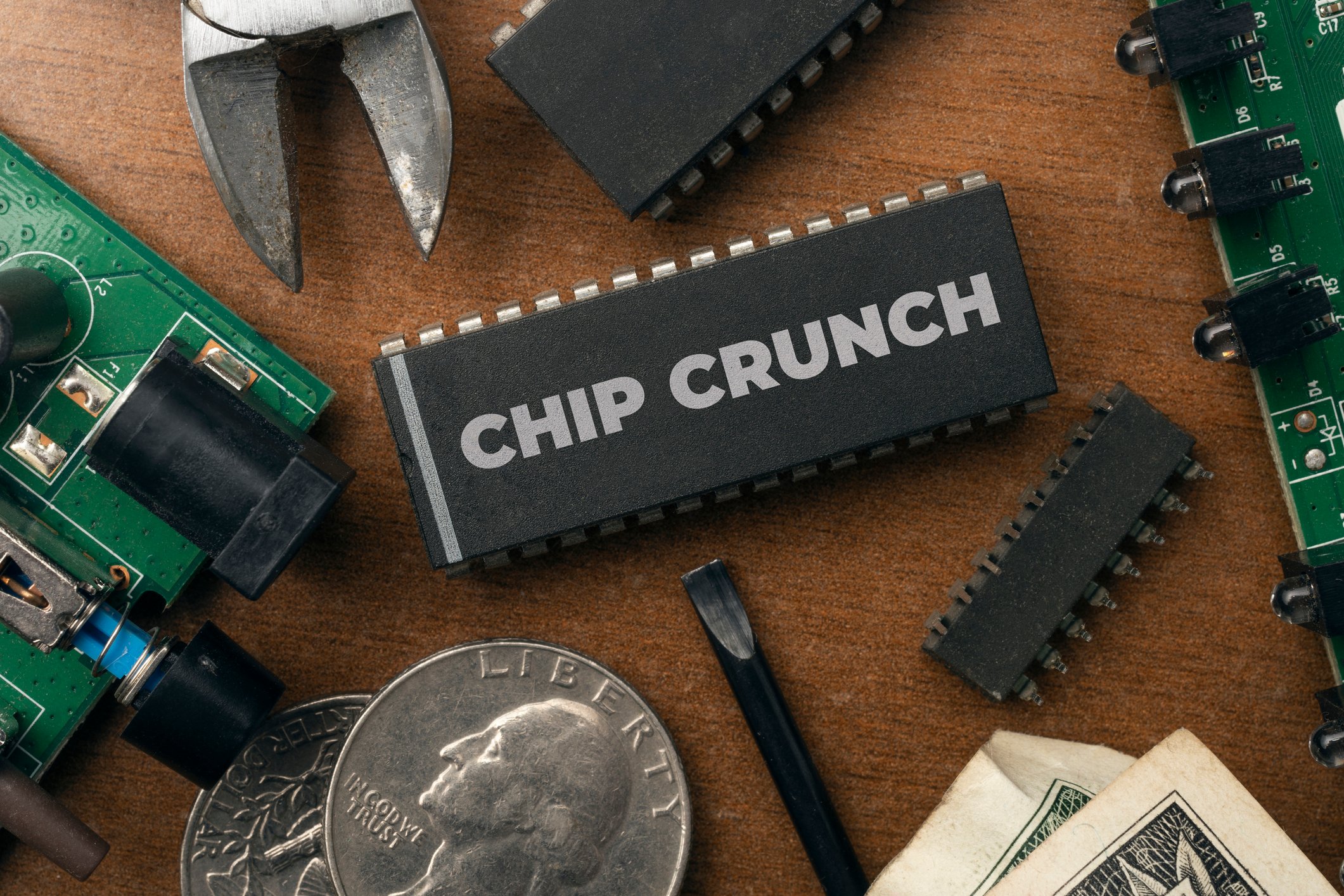 Circuit boards, coins, and tools on a table next to an electronics case that says chip crunch. 