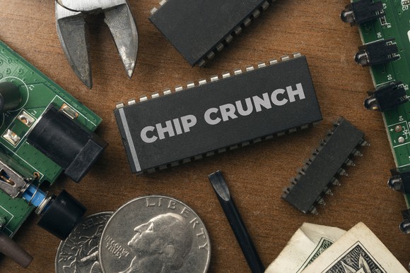 Circuit boards, coins, and tools on a table next to an electronics case that says chip crunch. 