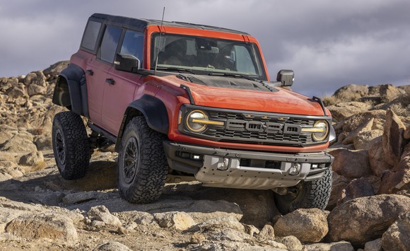 An orange 2022 Ford Bronco Raptor, an aggressive high-performance off-road SUV, shown traversing a rocky surface.